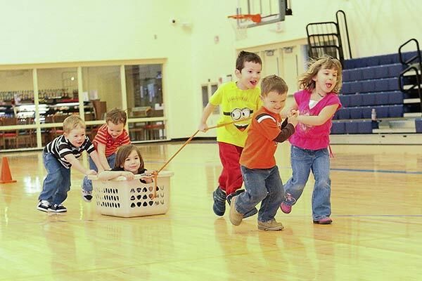 a group of children pulling another child in a basket, two other children push the basket