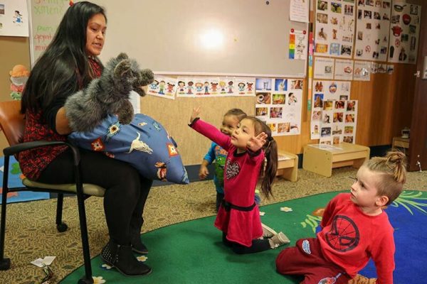 three children watching a teacher use a hand puppet