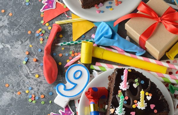 birthday party items on a table: balloons, candles, cake, gifts